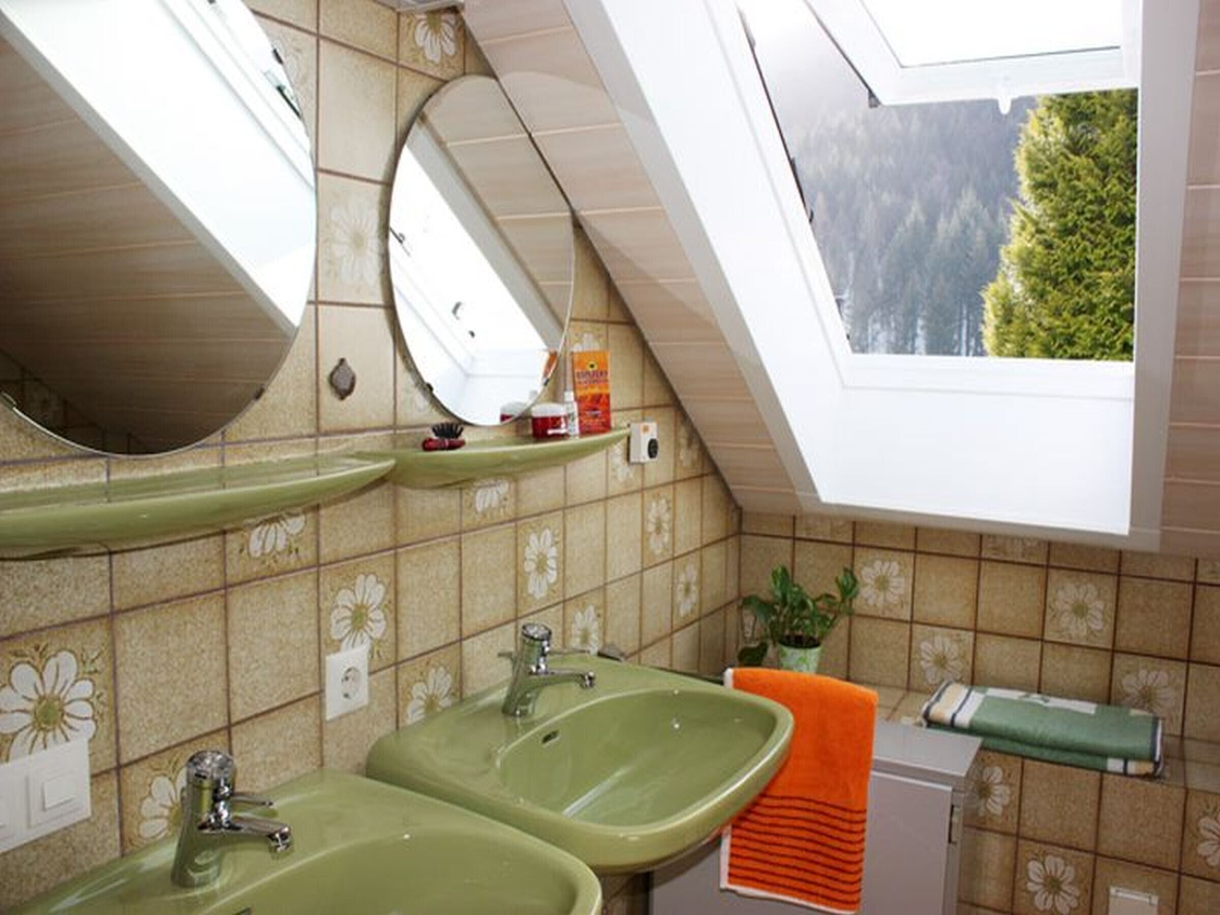 Een badkamer met twee groene wasbakken, een spiegel, een dakraam en uitzicht op bomen.