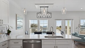 A modern kitchen with a large island, white cabinetry, and pendant lighting. - Riviera Sunrise - Chic, Modern, Pool and Beach Access (Panama City Beach)