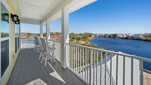 A covered deck with white railings, a pool, and a view of a river and distant buildings. - Riviera Sunrise - Chic, Modern, Pool and Beach Access (Panama City Beach)
