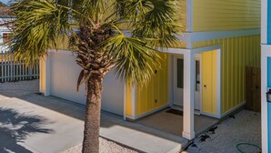 A two-story yellow building with a balcony on the upper floor, a palm tree in the foreground, and a clear blue sky. - Riviera Sunrise - Chic, Modern, Pool and Beach Access (Panama City Beach)