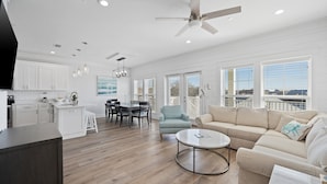 A spacious living area with a large sofa, a coffee table, and a dining area with a table and chairs. - Riviera Sunrise - Chic, Modern, Pool and Beach Access (Panama City Beach)