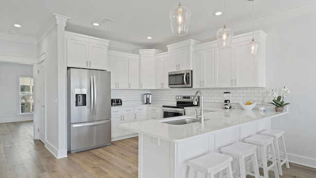 A modern kitchen with white cabinetry, stainless steel appliances, and a central island with bar stools. - Riviera Sunrise - Chic, Modern, Pool and Beach Access (Panama City Beach)