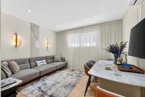 A modern living room with a sofa, a dining table, and a TV. - Seashell Diamond Luxury Suite (Playa San Juan)