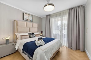 A modern hotel room with a large bed, a nightstand with a lamp, a framed picture on the wall, and a window with curtains. - Seashell Diamond Luxury Suite (Playa San Juan)