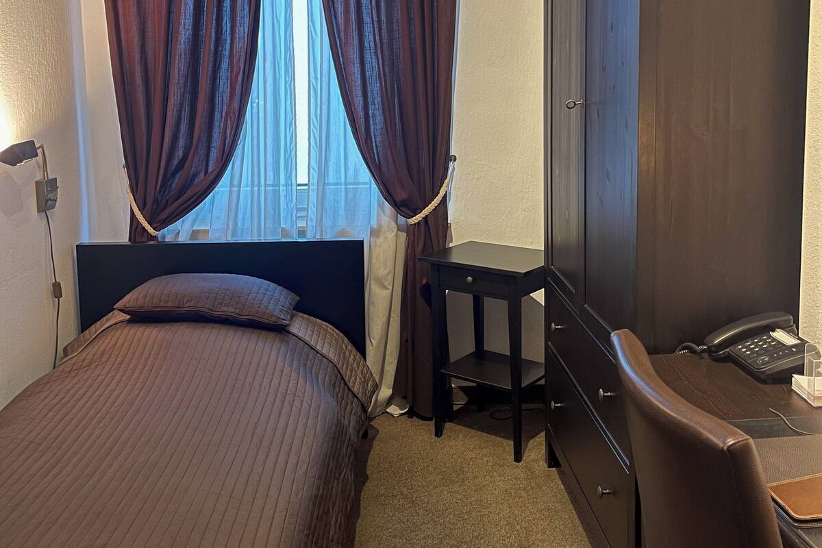 A hotel room with a bed, a desk with a telephone, and a wardrobe.