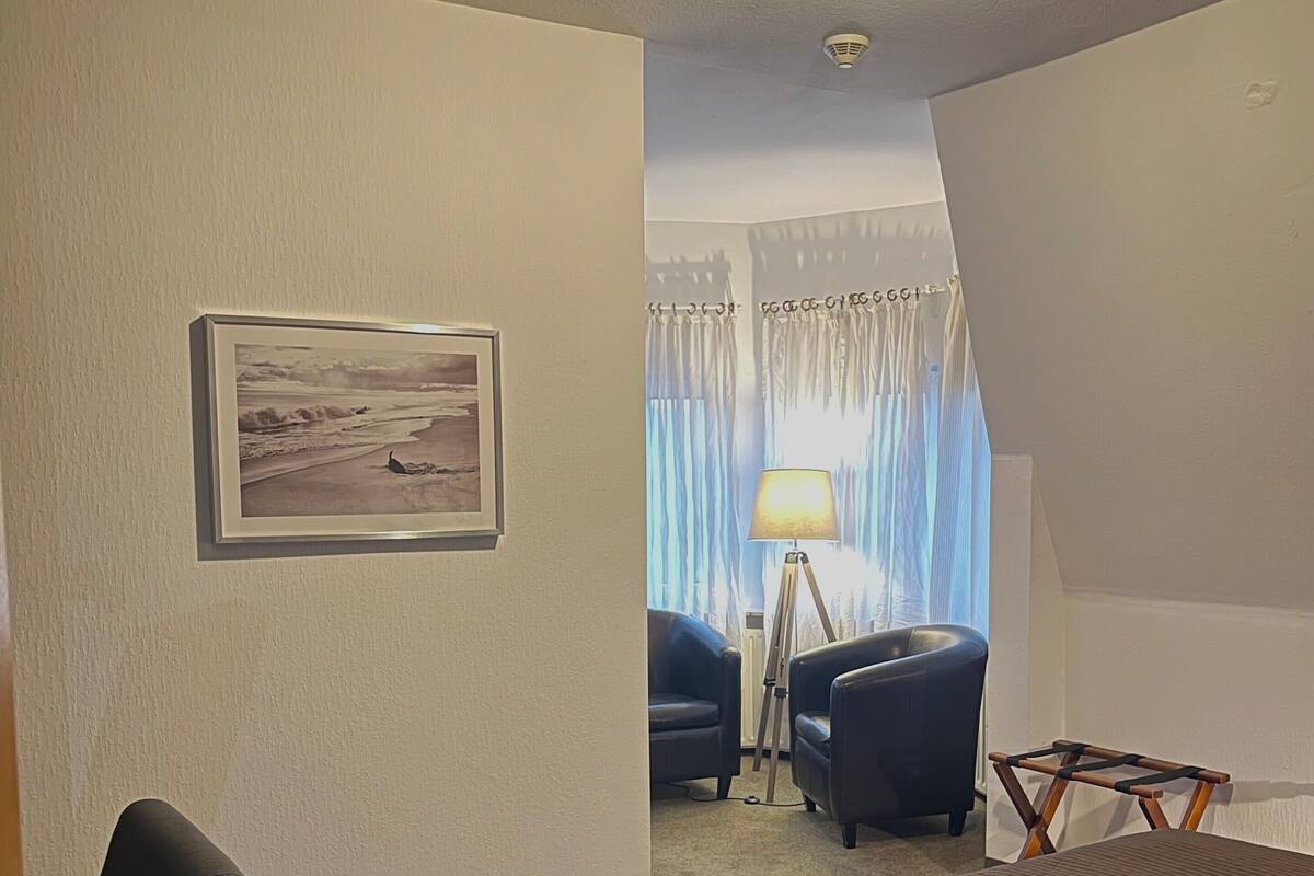 A hotel room with a bed, a chair, a desk, a lamp, and a framed picture on the wall.