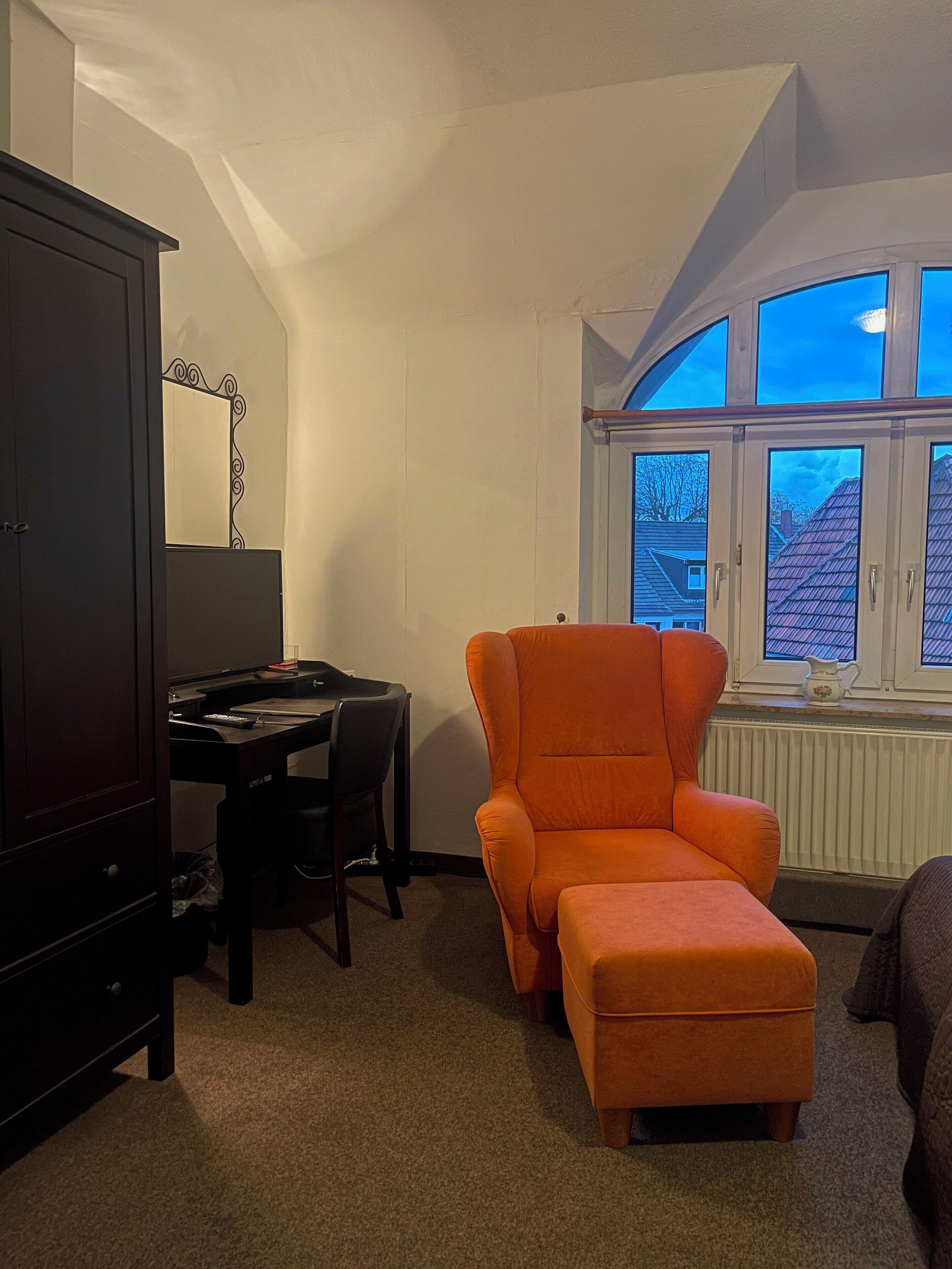 A room with a desk, chair, and an orange armchair.