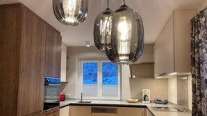 Une cuisine moderne avec des meubles en bois, un four encastré, une machine à café et une fenêtre équipée de stores.