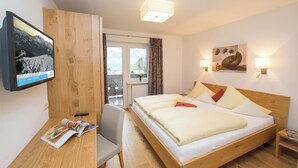 Une chambre d’hôtel avec un lit en bois, un bureau sur lequel se trouve un magazine, un téléviseur fixé au mur et un tableau au-dessus du lit.