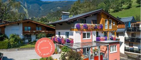 A hotel with a balcony with flower boxes, a covered outdoor seating area, and a view of the surrounding mountains.