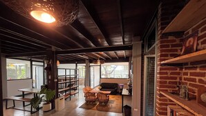 A spacious living area with a high ceiling, a fireplace, a bookshelf, and a dining area with a table and chairs.