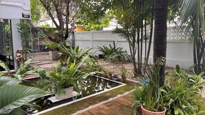 A garden with a pond, various potted plants, and a white fence.