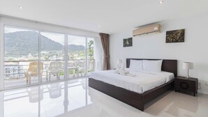 A modern hotel room with a large balcony, a bed, a nightstand, and a view of the city and mountains.