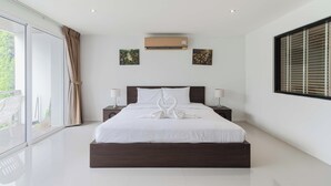 A modern bedroom with a large bed, two bedside tables, a window with blinds, and an air conditioning unit.