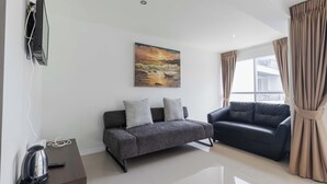 A modern living room with a grey sofa, a black sofa, a painting of a sunset, and a window with curtains.