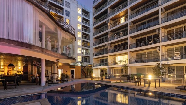 A multi-story hotel with a swimming pool, outdoor seating, and balconies.