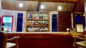 Zona de bar con vigas de madera en el techo, estantes con botellas de licores y dos sillas de madera.
