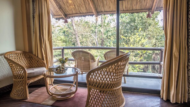 Un balcón con mobiliario de mimbre, una mesa de vidrio y vistas a árboles.