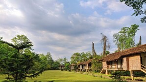 Una hilera de casas de campo con techos de paja y balcones de madera, rodeadas de abundante vegetación y un campo cubierto de césped.