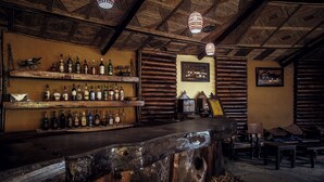 Un bar rústico con estantes de madera llenos de botellas, una barra de madera y un techo con vigas a la vista.