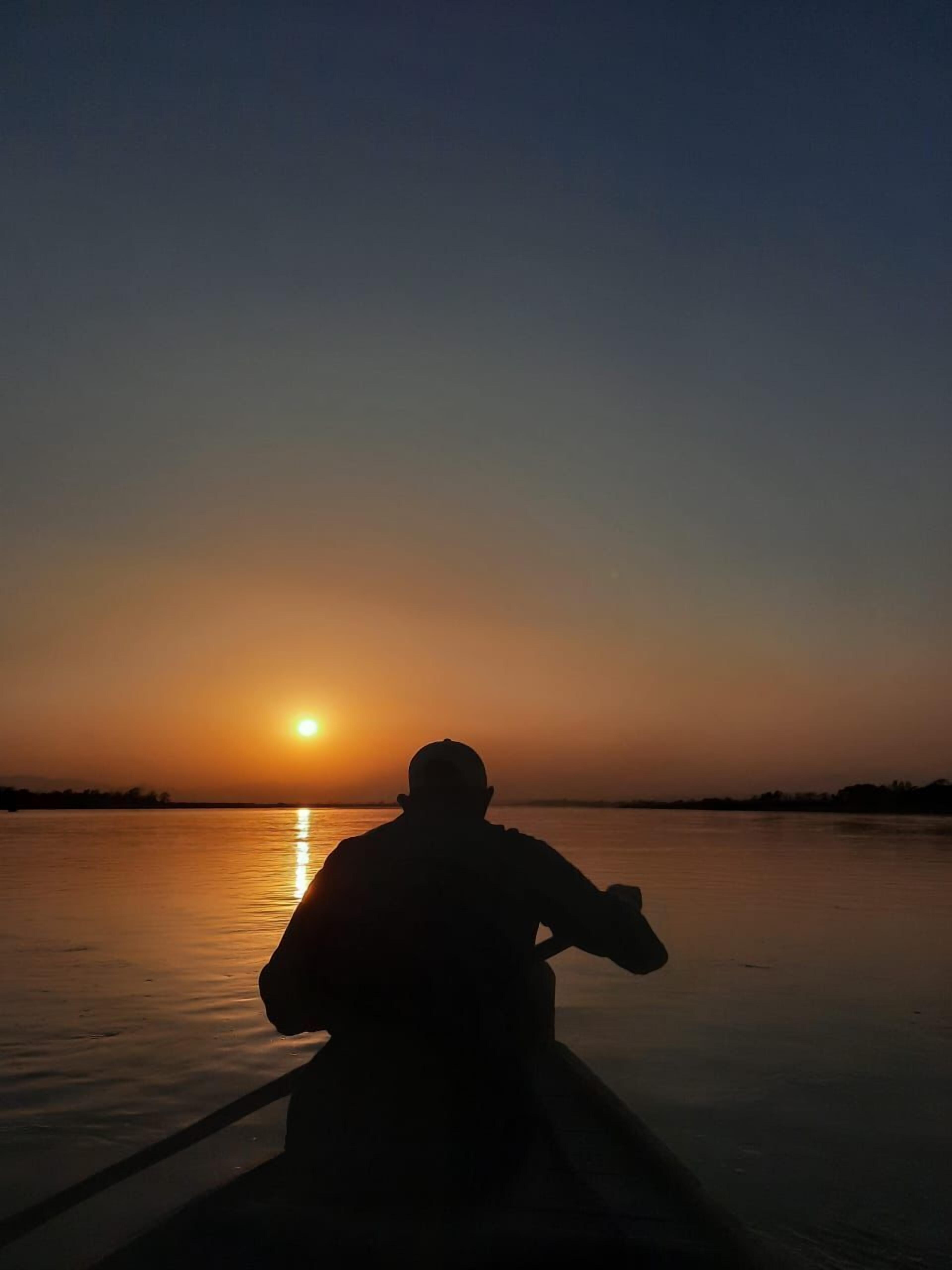 Una persona sentada en un bote al atardecer.