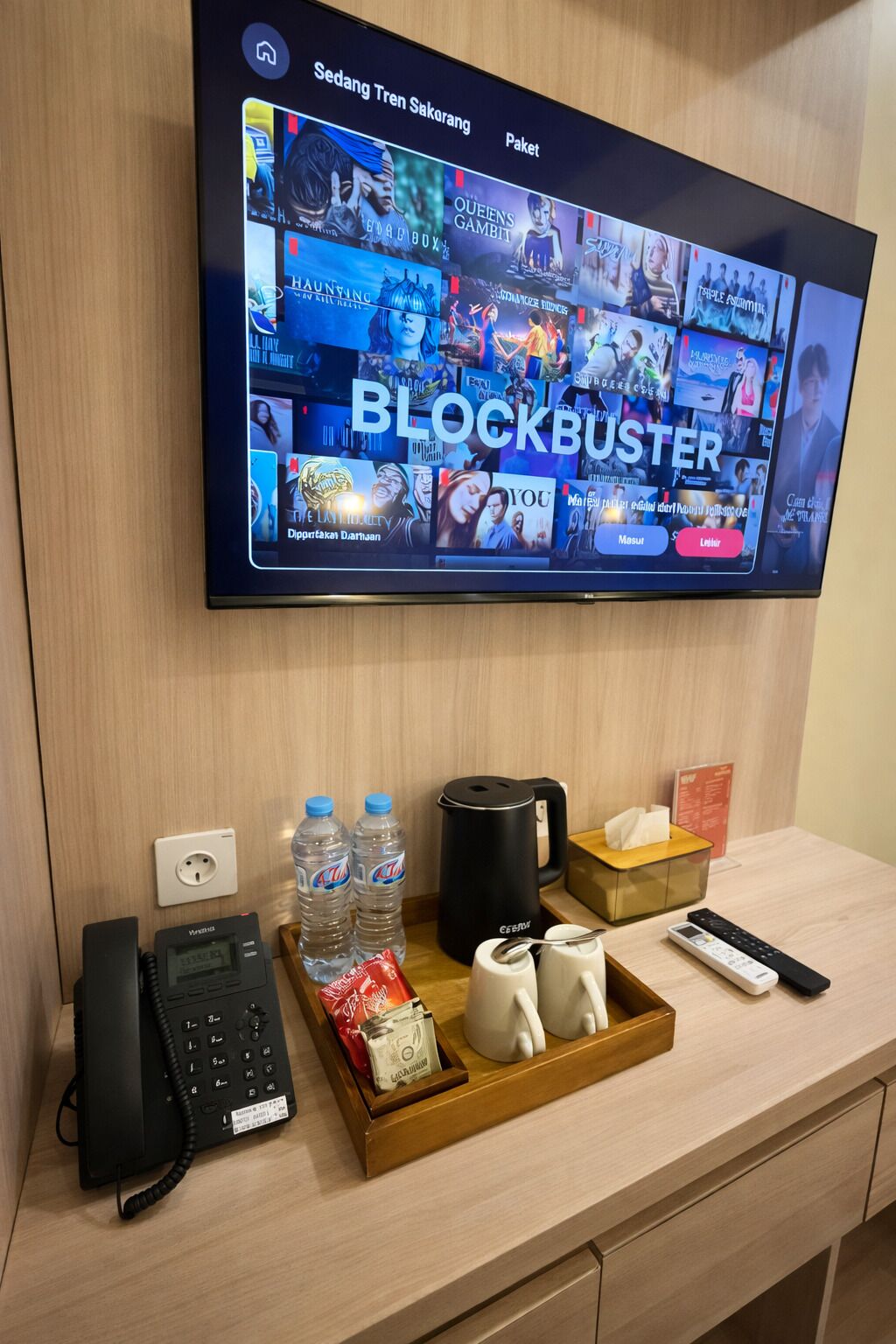 A hotel room with a flat-screen TV displaying a movie selection, a telephone, a tray with snacks, and a coffee maker.