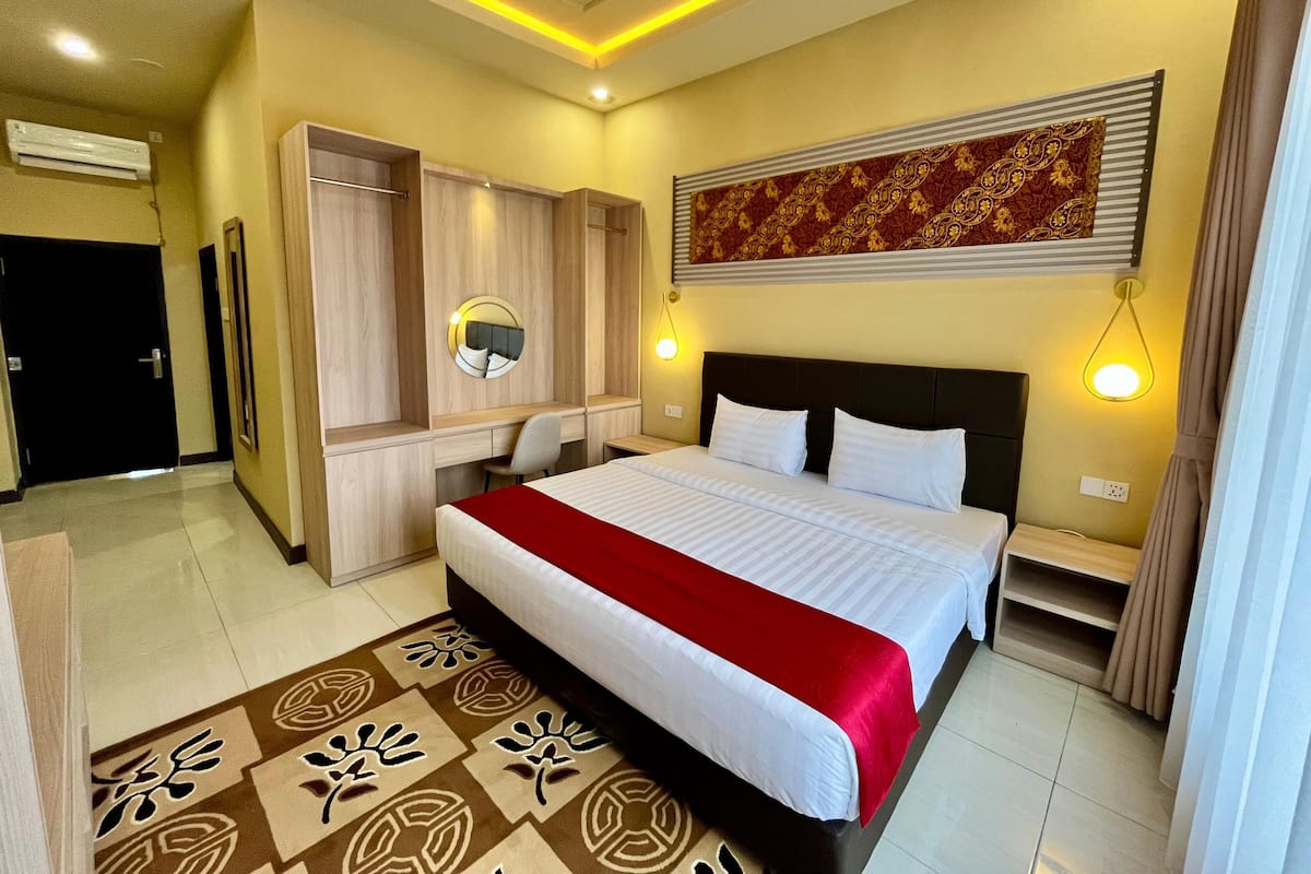 A hotel room with a large bed, a desk, a wardrobe, and a mirror.