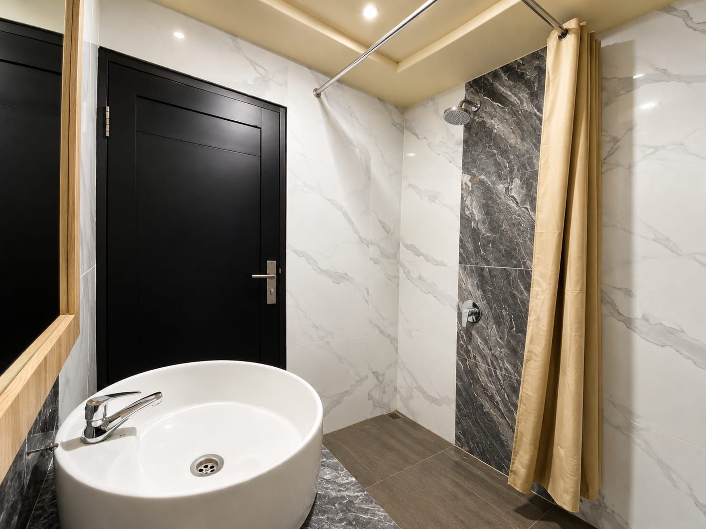 A bathroom with a white sink, a shower with a marble wall, and a black door.