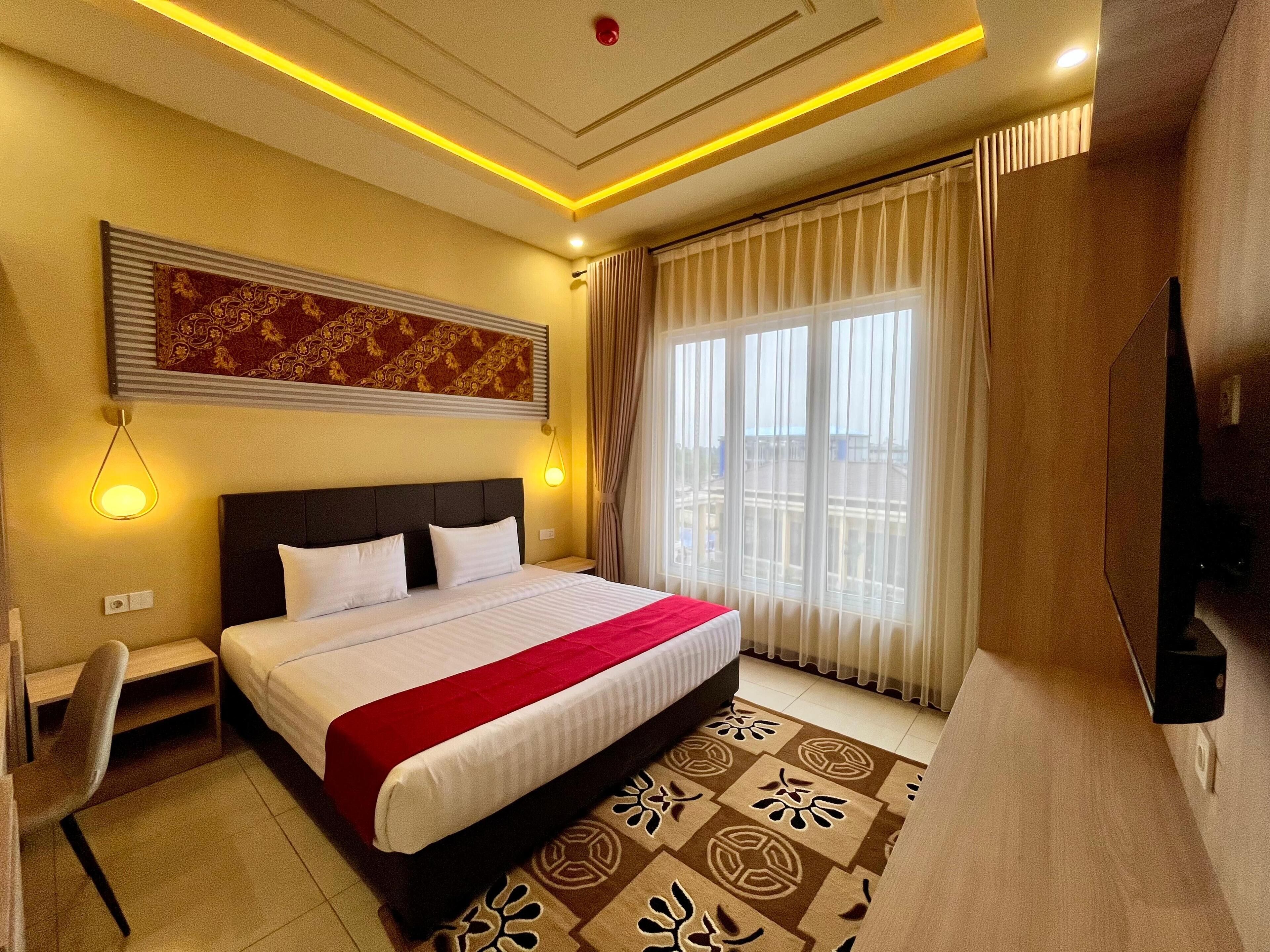 A hotel room with a large bed, a desk, a chair, a TV, and a window with curtains.
