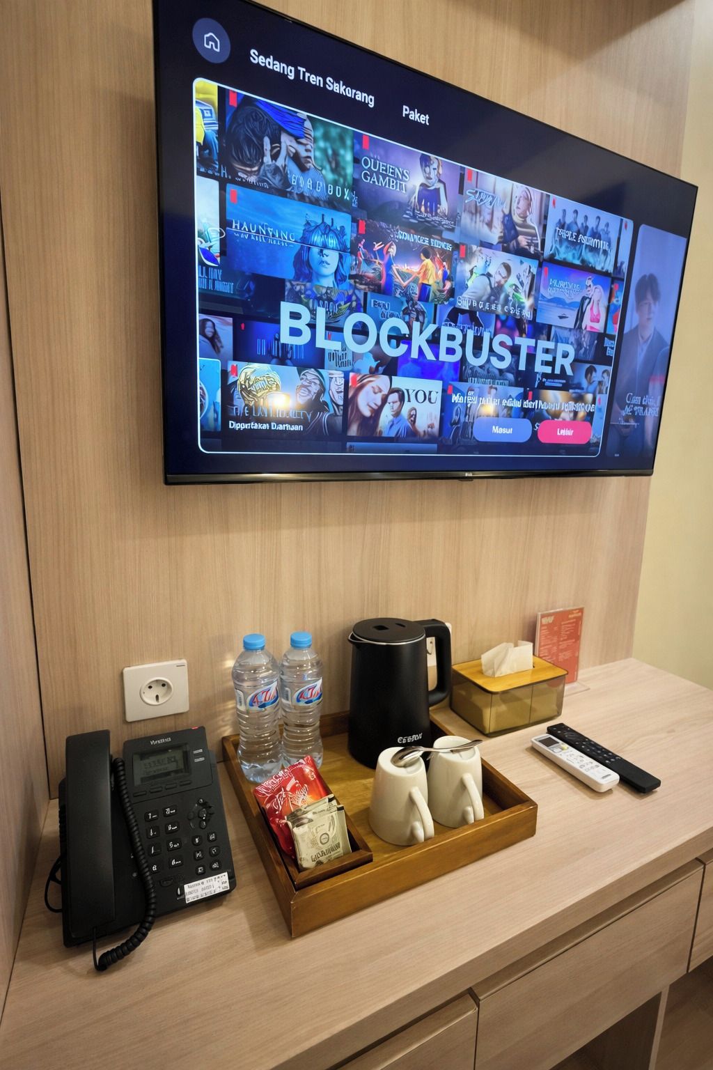 A hotel room with a flat-screen TV displaying a movie selection, a telephone, a tray with snacks, and a coffee maker.