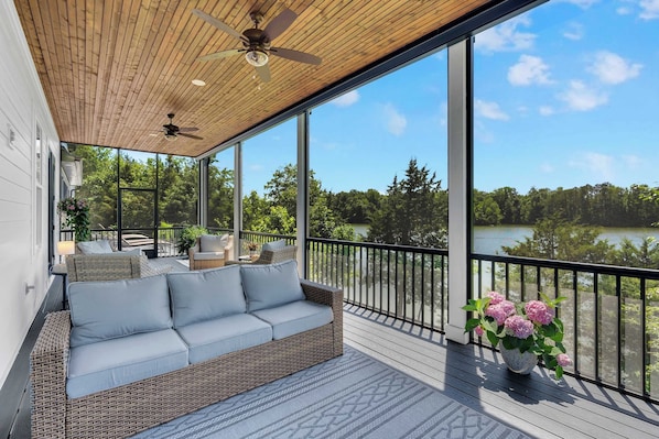 A balcony with a wicker sofa, a ceiling fan, and a view of a lake. - Lakefront Farmhouse | 14 Guests | Tims Ford Lake (Winchester)