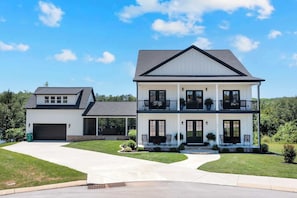 A two-story house with a garage, a covered front porch, and a landscaped lawn. - Lakefront Farmhouse | 14 Guests | Tims Ford Lake (Winchester)