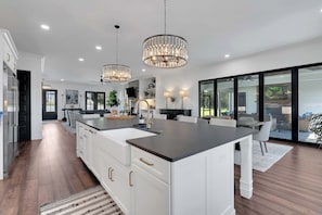 A modern kitchen with a large island, pendant lighting, and a view to the outdoor patio. - Lakefront Farmhouse | 14 Guests | Tims Ford Lake (Winchester)