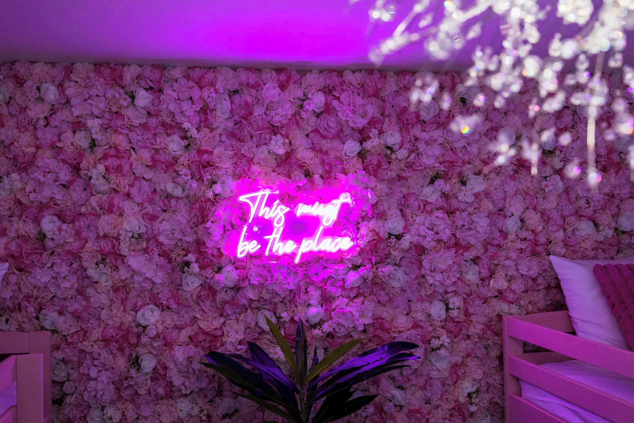 A room with a floral wall and a neon sign that reads "This is the place."