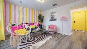 A room with a hanging chair, a sofa with colorful cushions, a zebra-patterned rug, and a yellow door.
