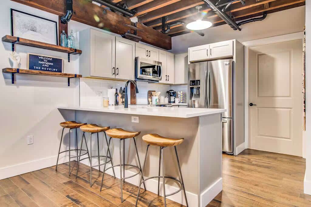 Una cocina moderna con armarios blancos, electrodomésticos de acero inoxidable y taburetes de madera.