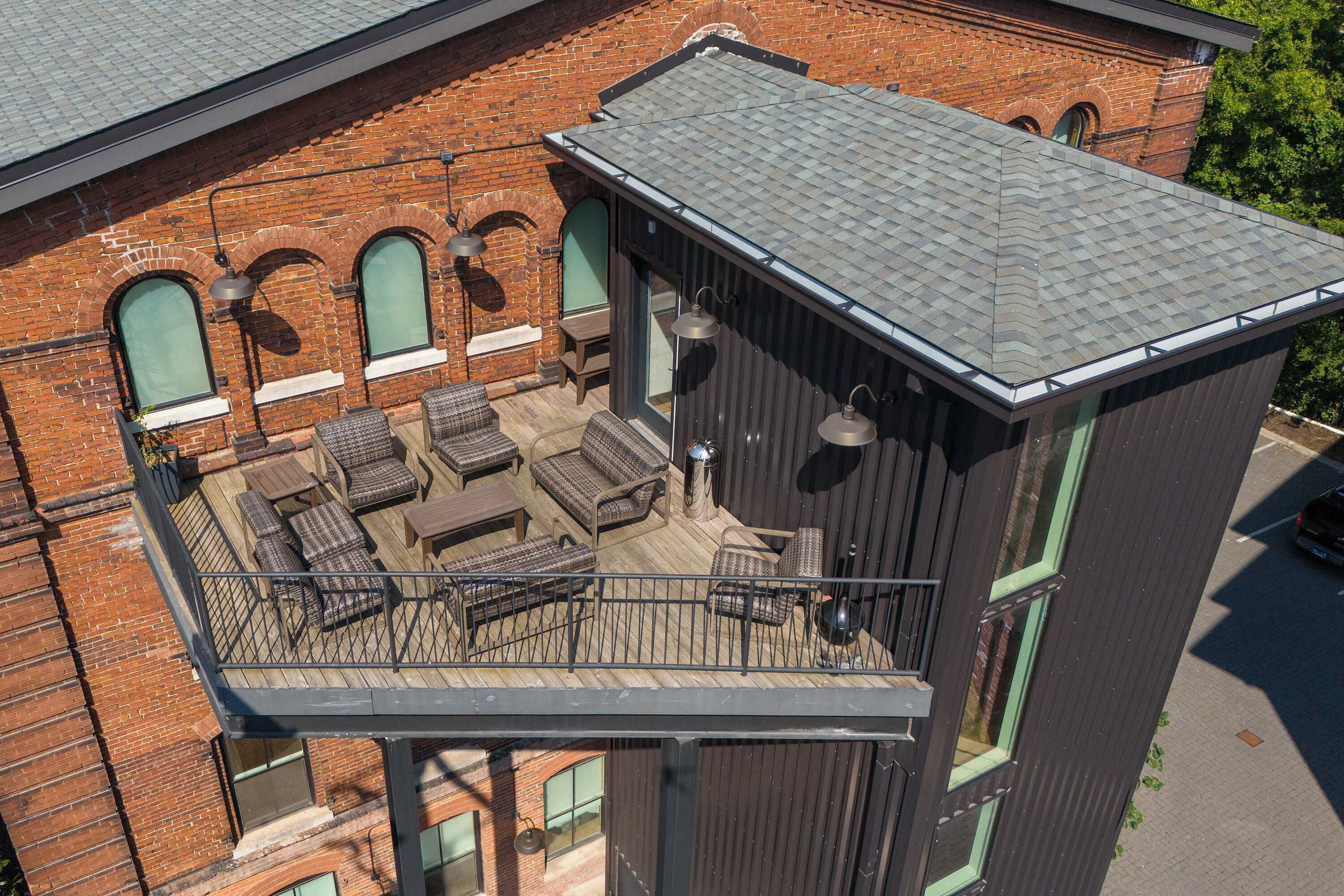 Une terrasse sur le toit, aménagée avec du mobilier d’extérieur et dotée d’une rambarde, est adossée à un bâtiment en briques avec des fenêtres en arc de cercle.