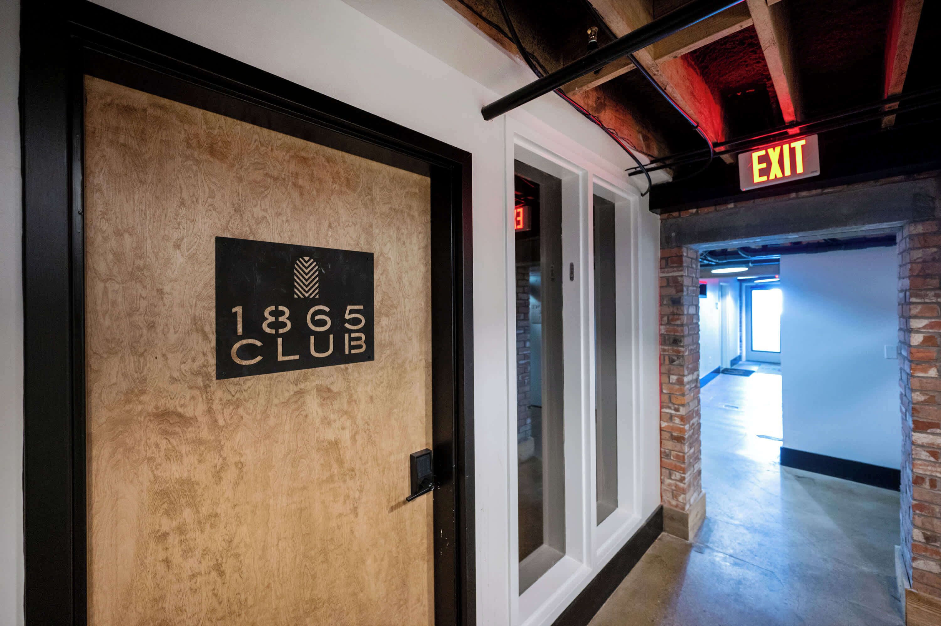 Un pasillo con una puerta que dice '1865 CLUB' y una señal de salida arriba.