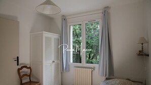 Een slaapkamer met een raam, een radiator, een stoel, een bed en een lamp.