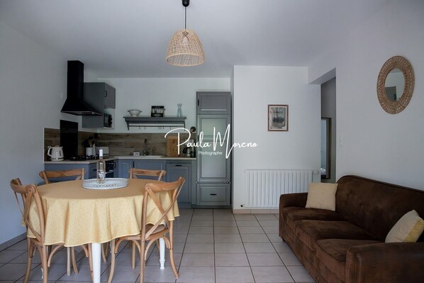 A modern kitchen with a dining table and chairs, a brown sofa, and a hanging light fixture.