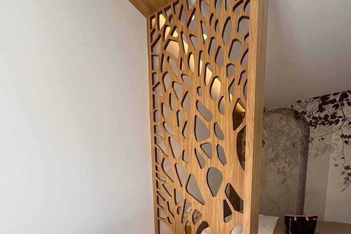 Un dormitorio moderno con un escritorio de madera, una computadora portátil, una taza, una silla y una cama con una manta y una bolsa.