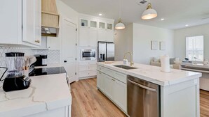 A modern kitchen with white cabinetry, a central island, stainless steel appliances, and pendant lighting. - Salt & Stone Villa 3425 (Galveston)