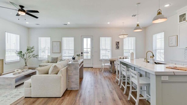 A spacious living area with a sofa, a coffee table, and a dining table with chairs. There is a kitchen area with a bar and a ceiling fan. - Salt & Stone Villa 3425 (Galveston)