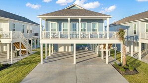 A two-story house with a balcony, a covered porch, and a small garden area. - Salt & Stone Villa 3425 (Galveston)