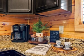 A kitchenette with a Keurig coffee maker, a potted plant, a WiFi sign, and a granite countertop. - Luxe Cabin • Pool • Hot Tub • Games • Pet Friendly (Pigeon Forge)