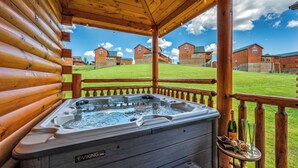 A wooden log cabin with a hot tub and a view of the surrounding buildings. - Luxe Cabin • Pool • Hot Tub • Games • Pet Friendly (Pigeon Forge)