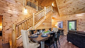 A wooden interior with a dining table set for four, a staircase, and a couch. - Luxe Cabin • Pool • Hot Tub • Games • Pet Friendly (Pigeon Forge)