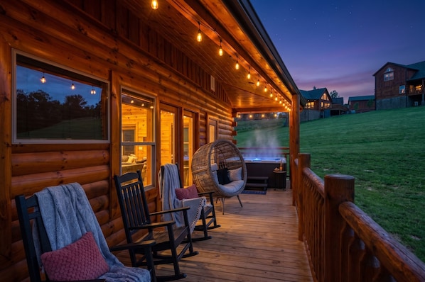 A wooden cabin with a deck, rocking chairs, and a hot tub.