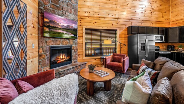 A cozy cabin interior with a stone fireplace, wooden walls, a dining area, and a kitchen. - Luxe Cabin • Pool • Hot Tub • Games • Pet Friendly (Pigeon Forge)