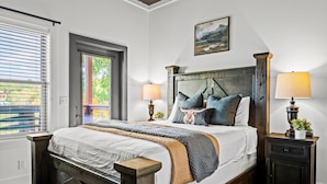 Une chambre avec un grand lit, deux tables de chevet, une fenêtre avec des stores et un tableau au mur.